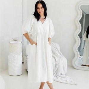 Woman wearing a white dress in a minimalistic room with a mirror and decorative items.