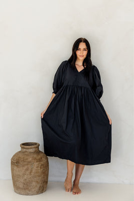 Woman wearing a black dress standing next to a large vase against a white background