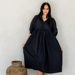Woman wearing a black dress standing next to a large vase against a white background