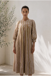 Woman wearing a striped dress standing against a white wall with a plant to the left.